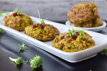 Broccoli balls deep fried on a white plate with tomato sauce with fresh broccoli on a black abstract background. Healthy eating concept. Dieting