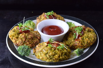 Broccoli balls deep fried on a white plate with tomato sauce with fresh broccoli on a black abstract background. Healthy eating concept. Dieting