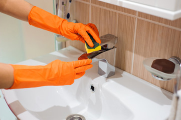 Hands in gloves with rubber cleaning bath faucet