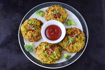 Broccoli balls deep fried on a white plate with tomato sauce with fresh broccoli on a black abstract background. Healthy eating concept. Dieting