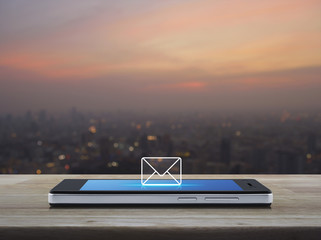 email icon on modern smart phone screen on wooden table over blur of cityscape on warm light...
