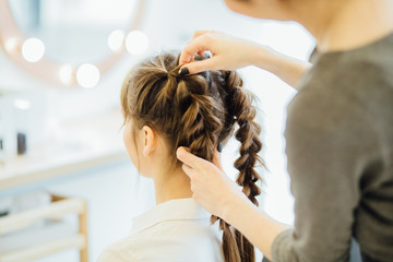 Naklejka premium Super styling. Close up of a hairdresser braiding her clients hair in trendy weave plait while sitting in hairdressing salon. European model. Beauty lifestyle concept.
