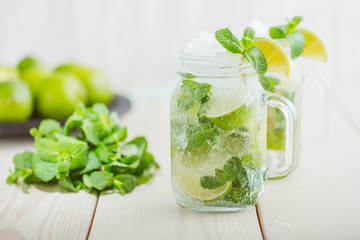 Two fresh mojitos cocktail in mason jar on wooden background. Mojitos with mint leaves, lime and ice. Drink making tools and ingredients for cocktail.