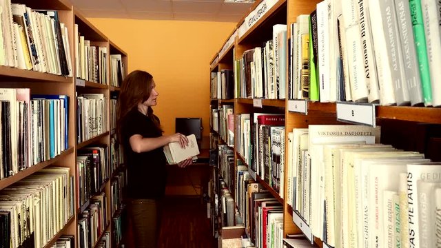 Young female librarian girl putting books in wooden library shelf