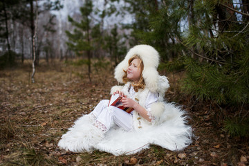 A boy in a white fur hat  outside warming in the forest in spring 