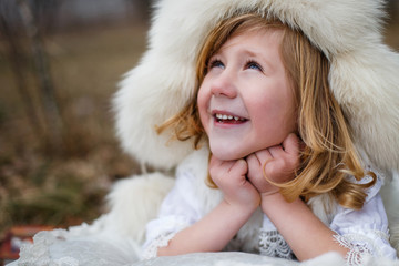 A boy in a white fur hat  outside warming in the forest in spring 