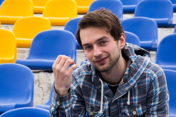 Attractive sporty young man model in blue shirt sitting on blue stadium seats after training staring at field