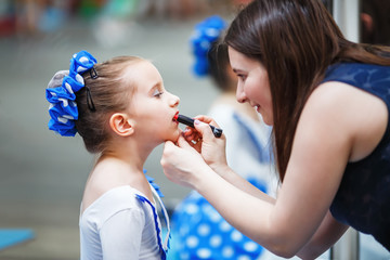 Mom paints lips with the lipstick of her little daughter before the dance performance. Mother makes...