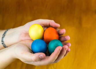 Four bright eggs painted for the Easter holiday lie in the palms of the hands on a wooden background close-up