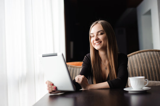 Happy young woman drinking coffee / tea and using tablet computer in a coffee shop
