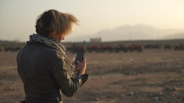 Cute blonde woman trying to make a selfie in the desert slow mtoion