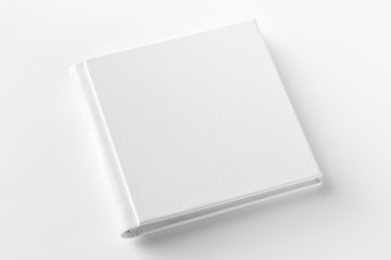 Mockup of closed blank square book at white textured paper background. Angle view