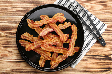 Plate with tasty bacon slices on wooden background