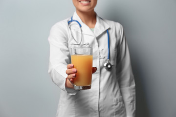 Female nutritionist with glass of juice on light background, closeup