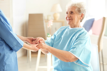 Young doctor holding hands of elderly woman on light background