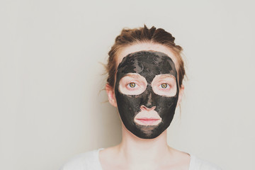 Close-up portrait of attractive girl with a black mask on the face. Skin care.
