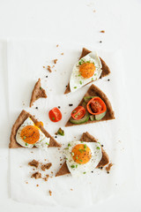 Slices of pie similar to pizza with vegetables, egg and avocado lie on white background, top view.