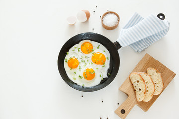 Fried scrambled eggs in a frying pan, bread and salt on a white background.