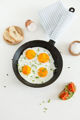 Fried scrambled eggs in a frying pan, bread and salt on a white background.
