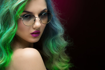 Fototapeta premium She is not an ordinary one. Closeup portrait of a beautiful female fashion model with green hair wearing glasses looking over the shoulder seductively