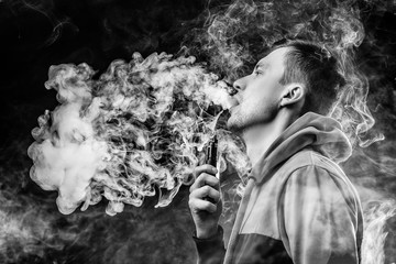 Vape. Young handsome white guy is admiting puffs of steam from the electronic cigarette.Black and white photo.