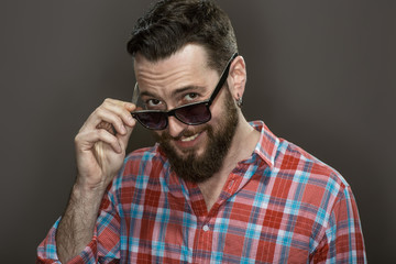 Obraz premium Hey you! Stylish bearded guy wearing glasses looking to the camera smiling on dark background at the studio.