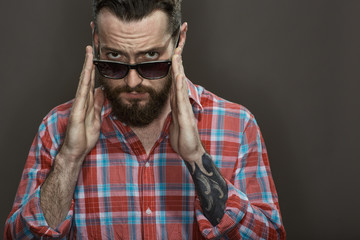 No jokes. Cropped shot of a bearded tattooed guy holing his glasses looking to the camera confidently on black background at the studio.