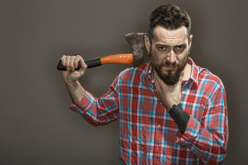 How to be a real man. Studio portrait of a bearded man looking seriously to the camera carrying an axe on his shoulder on grey background.