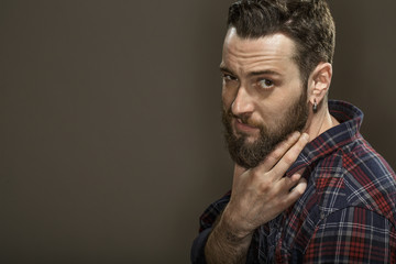 He knows you like him. Portrait of a bearded guy looking to the camera confidently touching his beard copyspace on the side on grey background.
