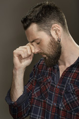 Fototapeta premium Need a rest. Portrait of a disappointed bearded man touching his face with his eyes closed at the studio on grey background.