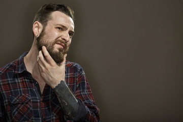 To shave or not to shave. Studio portrait of a handsome bearded man scratching his beard thoughtfully copyspace on the side on grey background.