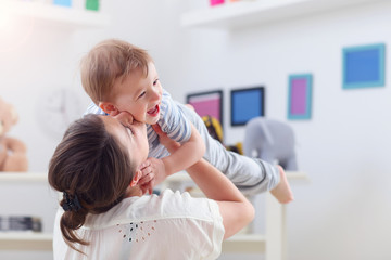 Happy mother playing with baby boy at home
