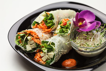 Beautiful view of a plate of spring rolls with sweet chili sauce; styled on black plate