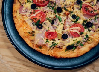 Large hot pizza on the black plate.