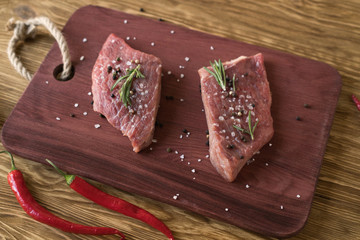 Fresh raw steaks with rosemary and pepper on wooden desk