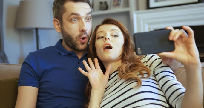 Happy young cuple relaxing on the sofa and taking selfies in a living room. Taking a selfie. Making funny faces