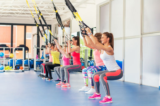Group of beautiful young women working out on TRX and smiling.