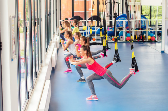 Group of beautiful young women working out on TRX and smiling.