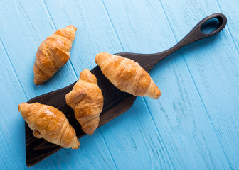 Delicious fresh mini croissants on wooden cutting board on blue background. Healthy Breakfast with copy space. Top view.