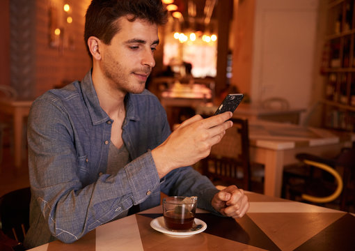 Cute millenial male texting in restaurant
