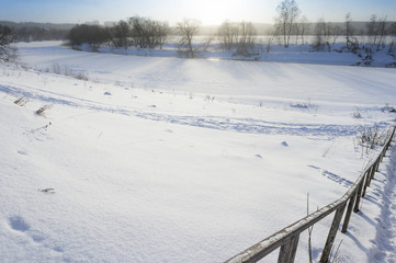 beautiful winter rural landscape with river, steep bank, trees, wooden stairs and snow