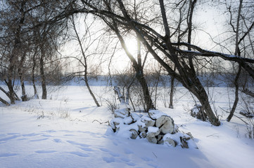 beautiful winter rural landscape with river, trees, a bundle of firewood and snow