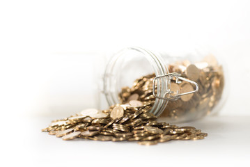 Overturned glass pot full of shined Golden coins on the white background