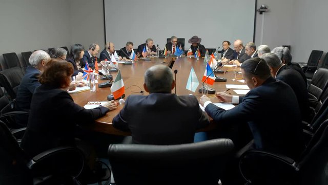 Political negotiations at international business forum or summit. Diverse group of people in suits start discussing at the round table in conference hall