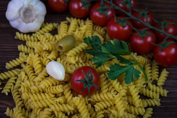 Pasta with cherry tomato, parsley, garlic and olives on a wooden background