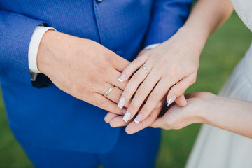 Groom in a blue suit and bride in a white dress holding hands on the fingers of the bride and groom wedding rings