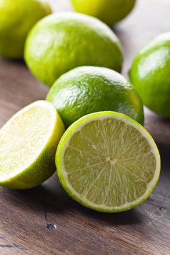 Group of whole and cut fresh limes on a wooden table .