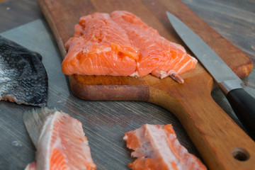 Salmon fish being splitted on wooden desk. Salmon fillet, filler trimmings, fin, skin, fish scale, kitchen desk, knife. Top view.