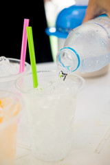 pouring water in transparent plastic cups with straw.
