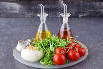 Ingredients for the traditional Italian caprese salad on a glass tray on a grey background with bottles of olive oil and wine vinegar.